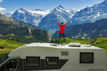 Dieser Outdoor-Abenteurer genießt die atemberaubende Bergkulisse vom Dach seines Campers aus